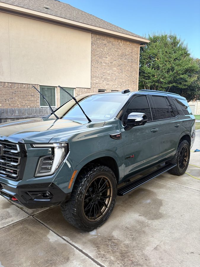 Dark green GMC Yukon AT4 on bronze wheels finished to a deep gloss in a driveway